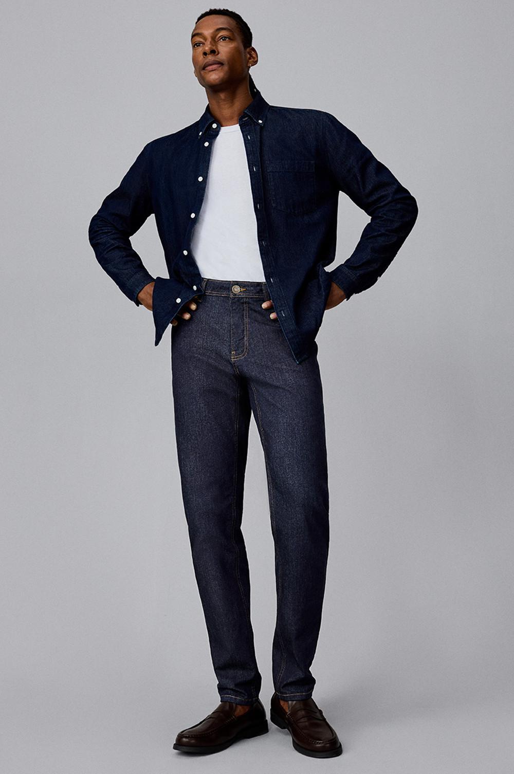 Personne posant avec une chemise bleu marine en denim sur un t-shirt blanc et un jean foncé avec des mocassins marron.