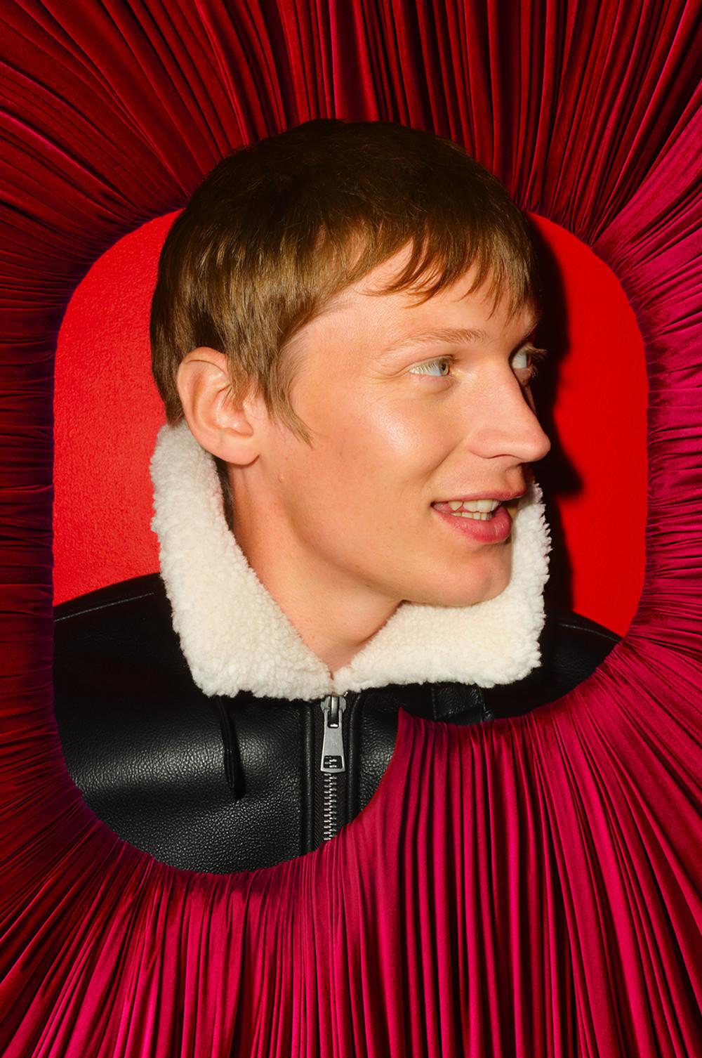 Persona che indossa una giacca di pelle nera con collo in sherpa bianco circondata da un vistoso tessuto pieghettato rosso.