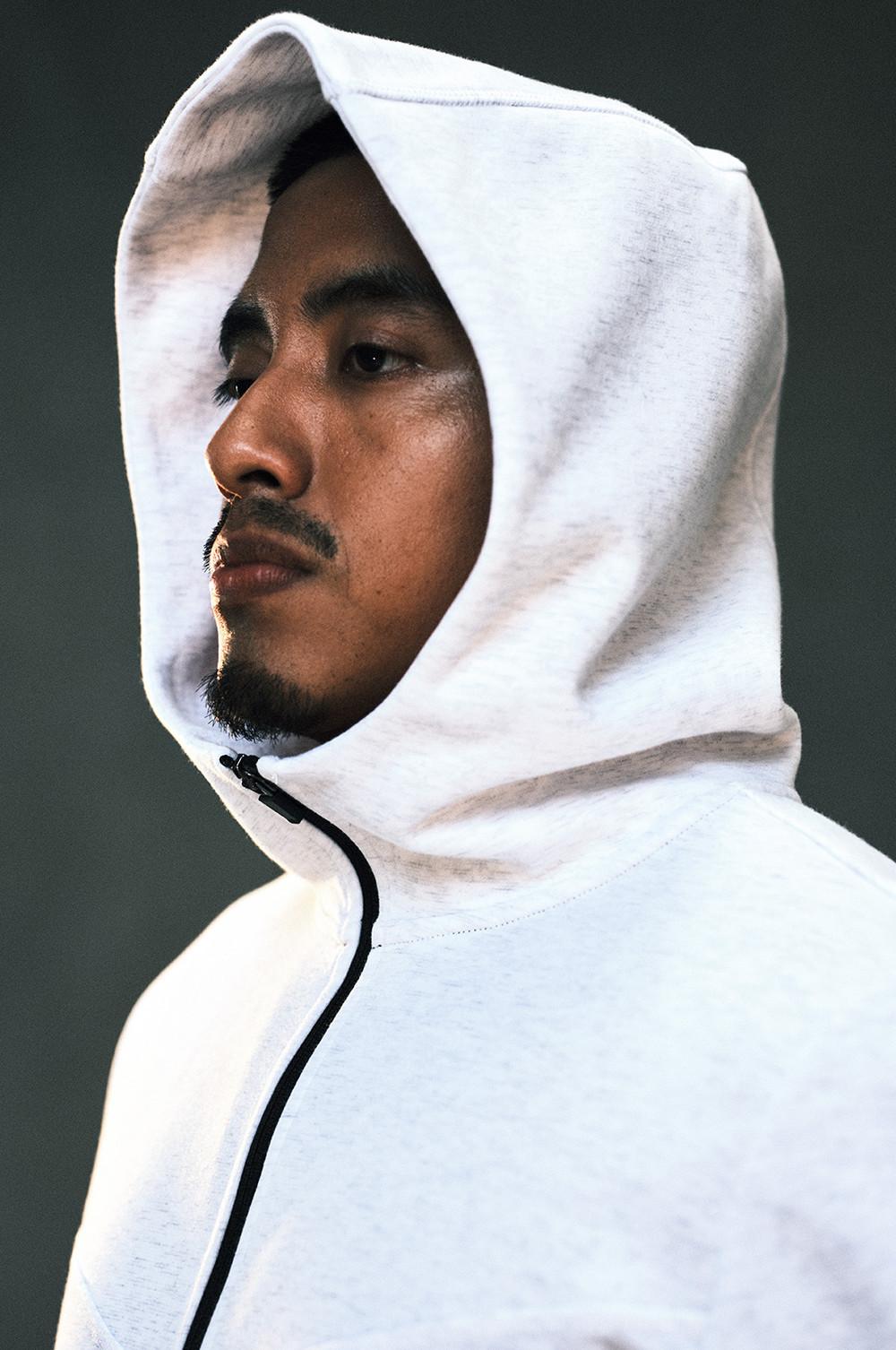 Profile view of person wearing a white hoodie with black drawstring against a dark green background.