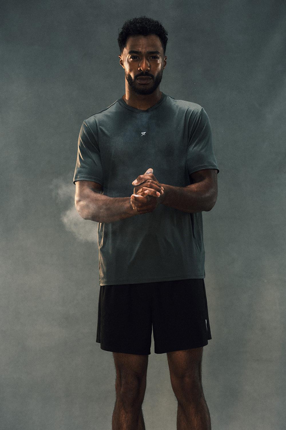 Person wearing grey athletic t-shirt and black shorts standing in misty atmosphere.