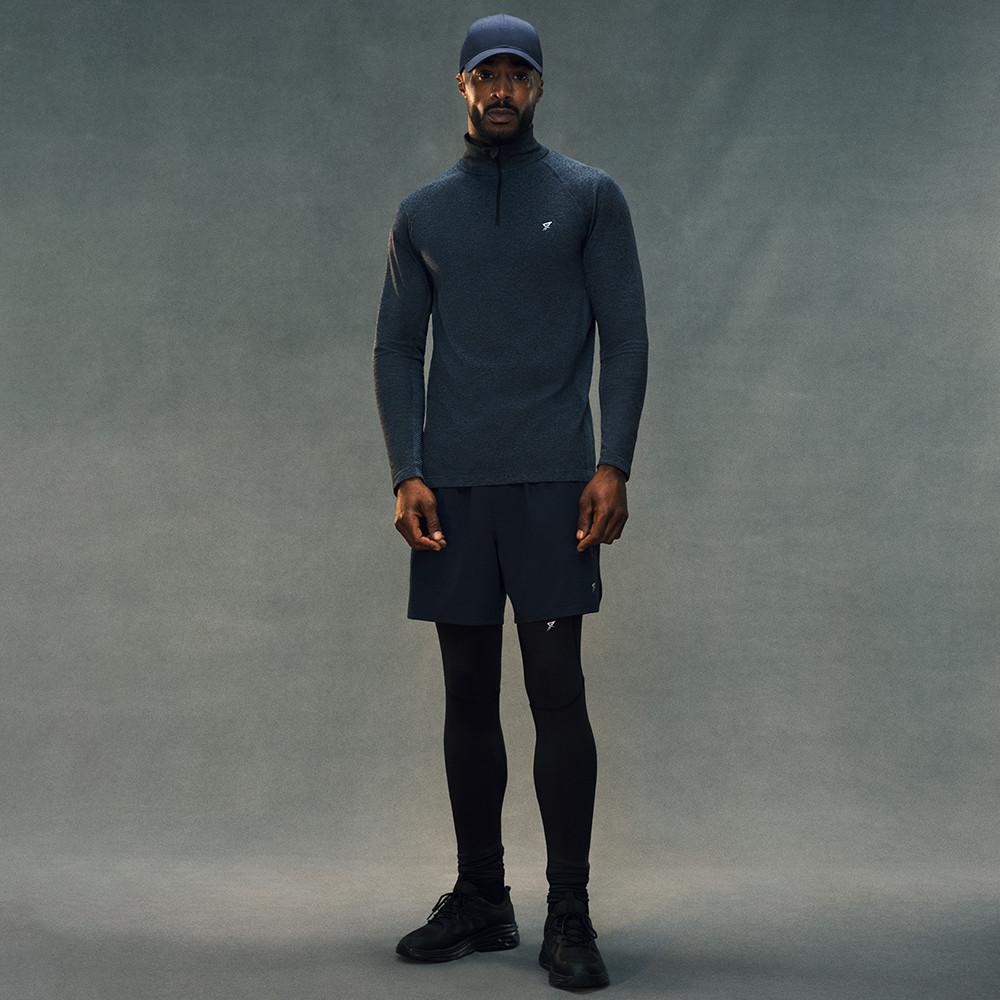 Person wearing dark sportswear including quarter-zip top, shorts over leggings, cap and trainers.