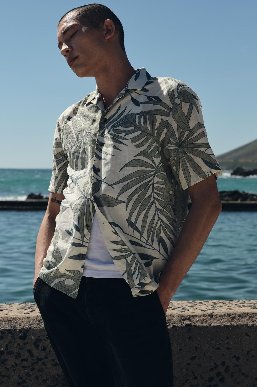 Model wearing a palm tree print shirt, white t-shirt underneath with black shorts