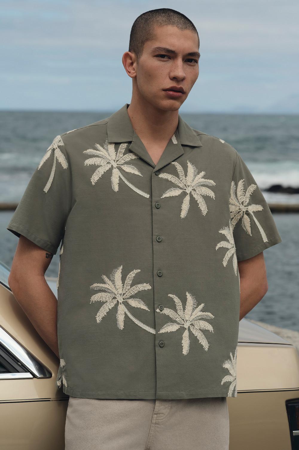Model wearing a palm tree print khaki shirt with grey trousers