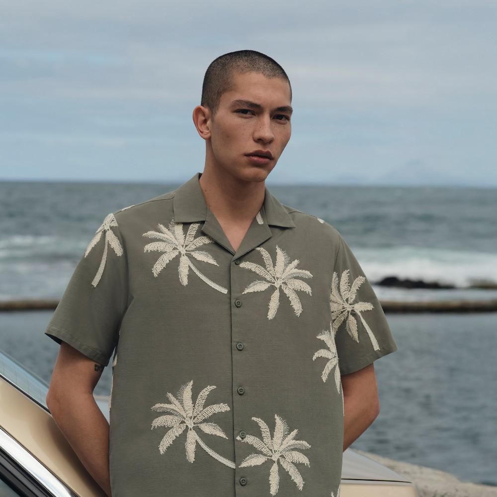 Model wearing a khaki palm tree print shirt