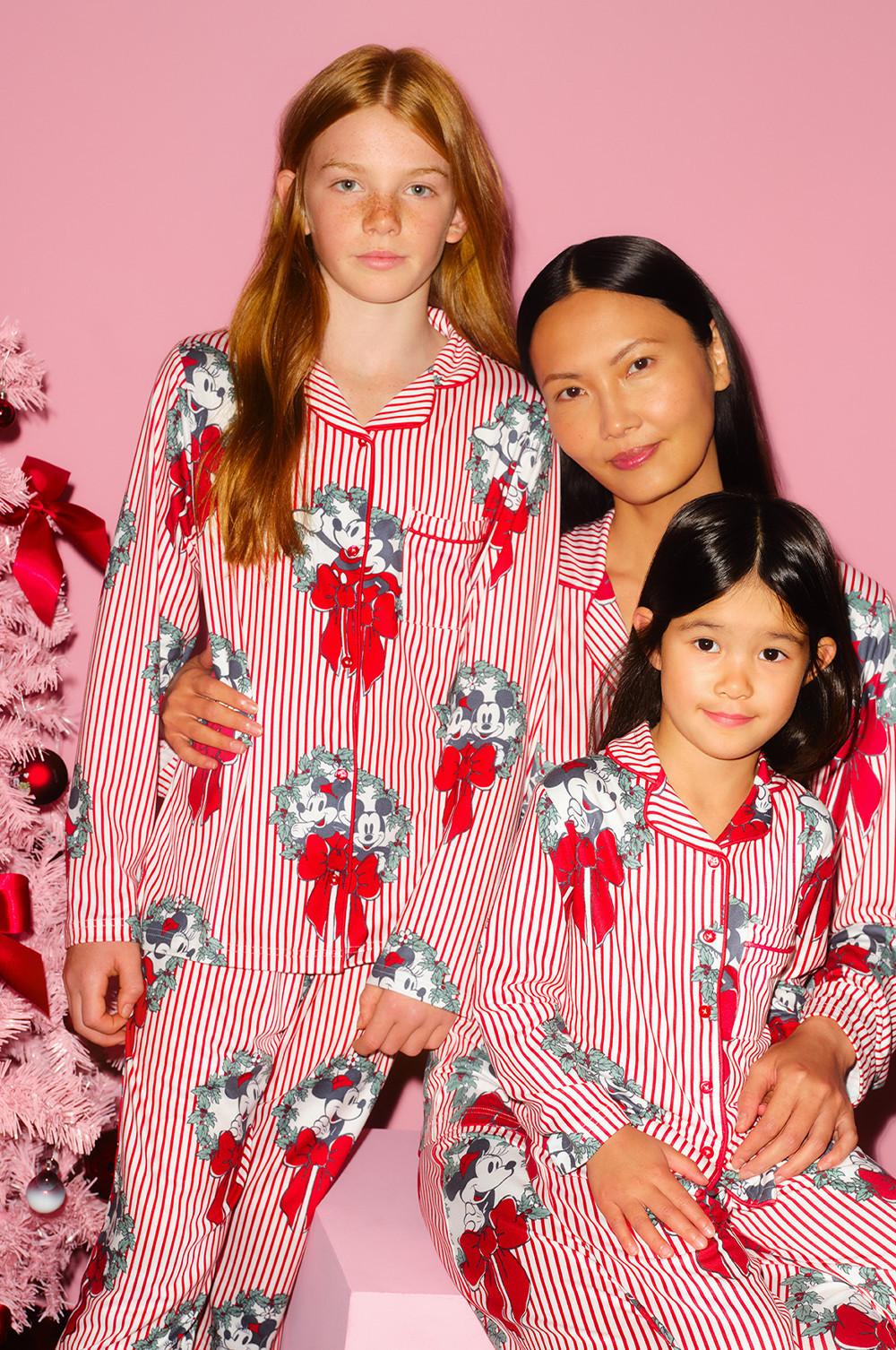 Three people wearing matching Disney Mickey Mouse striped pajamas with festive decorations beside a pink Christmas tree.