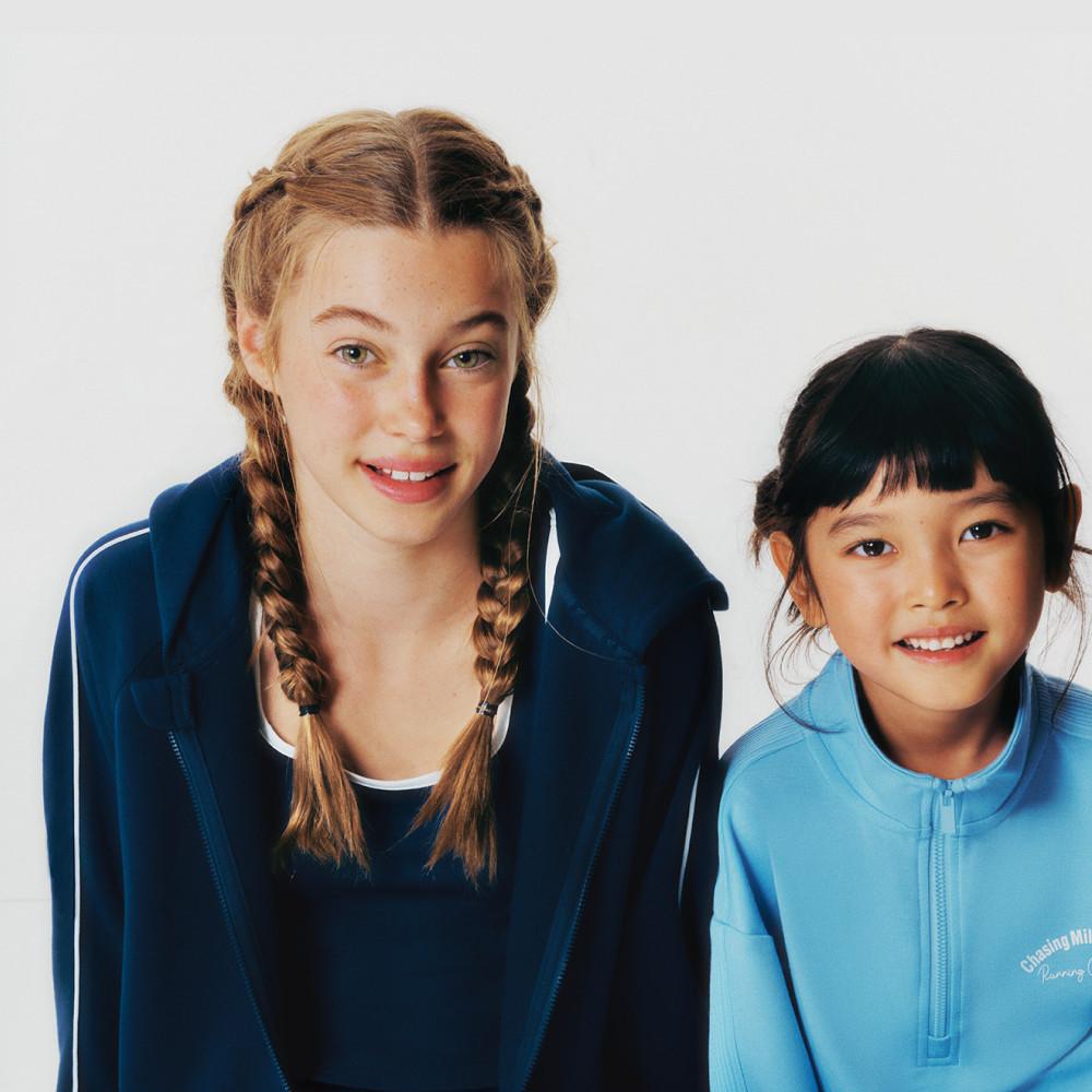 Two children wearing sportswear - navy blue and light blue zip-up tops against a white background.