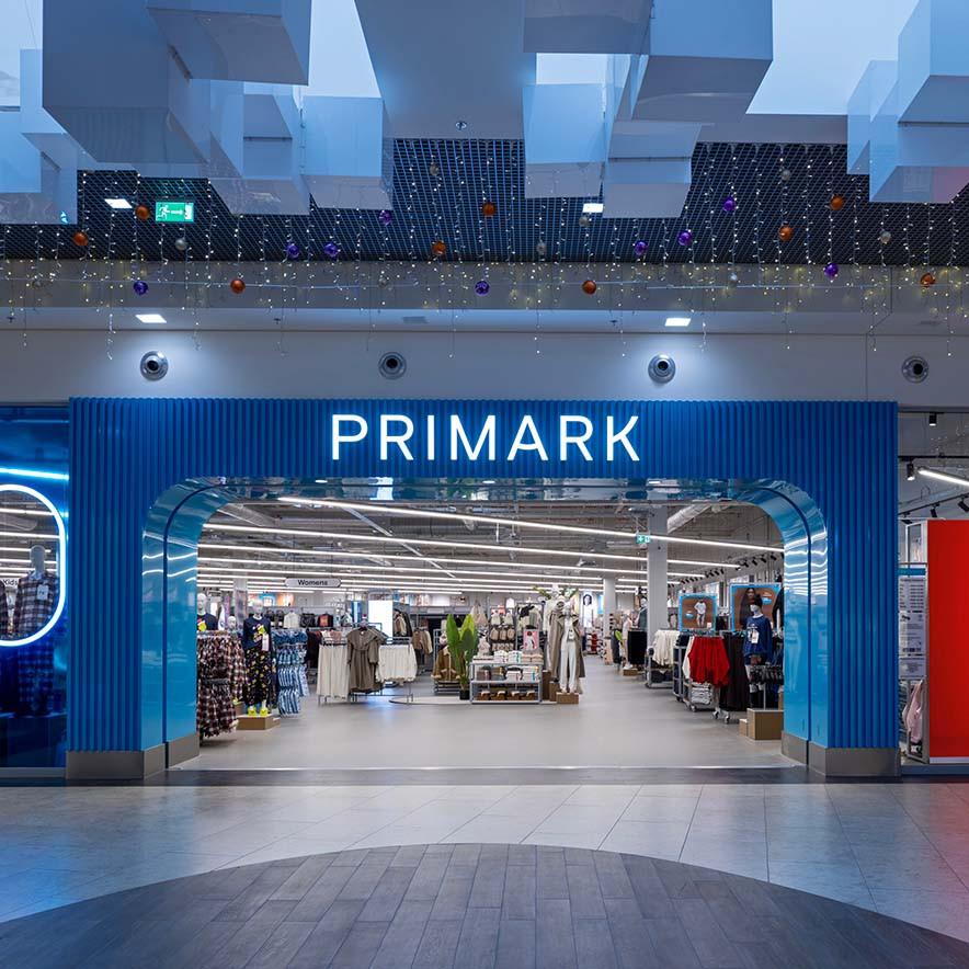 The storefront of a Primark retail shop with a blue arched entrance and neon signage.