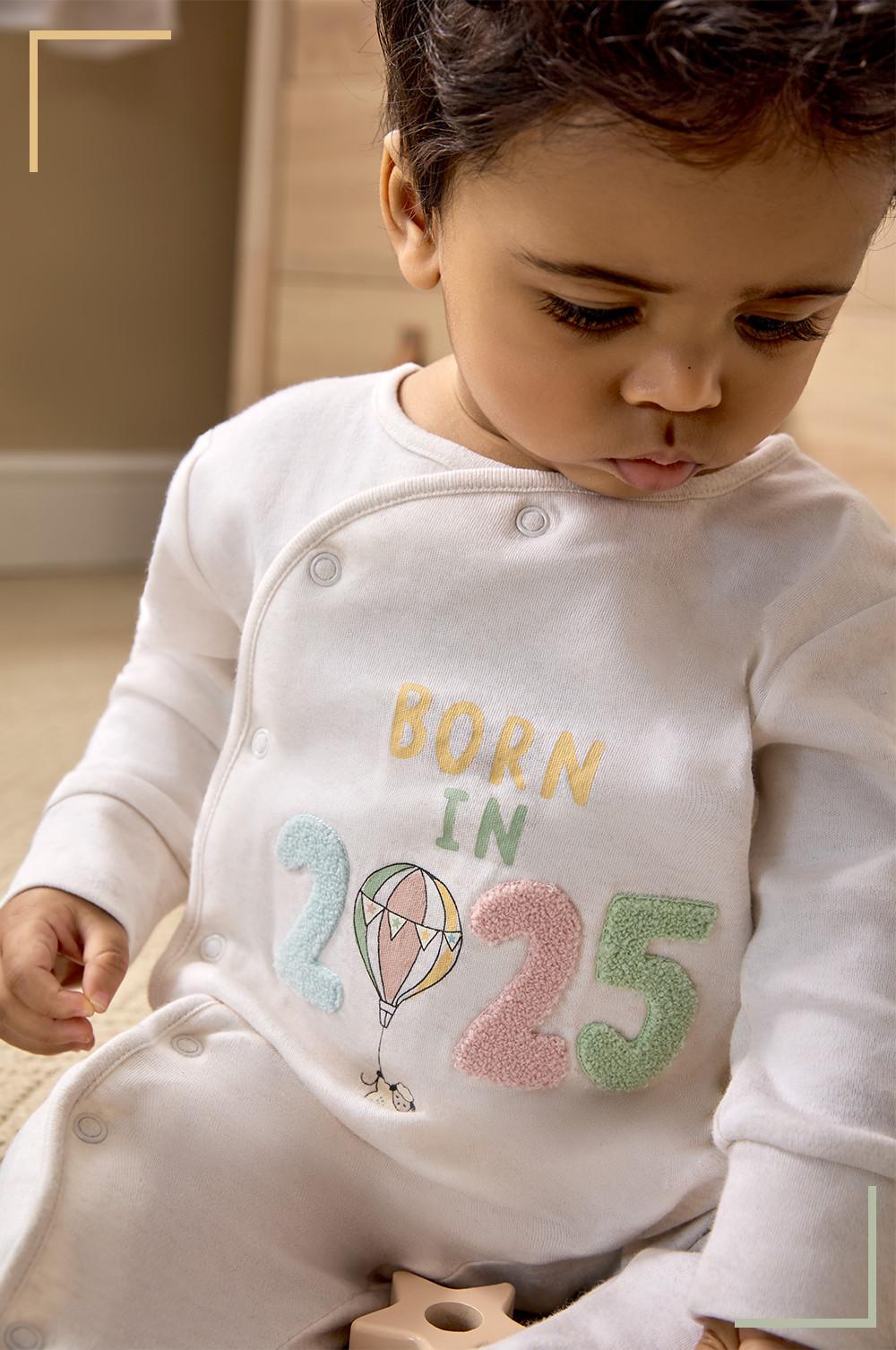 Grenouillère blanche avec inscription « BORN IN 2025 » et motif montgolfière