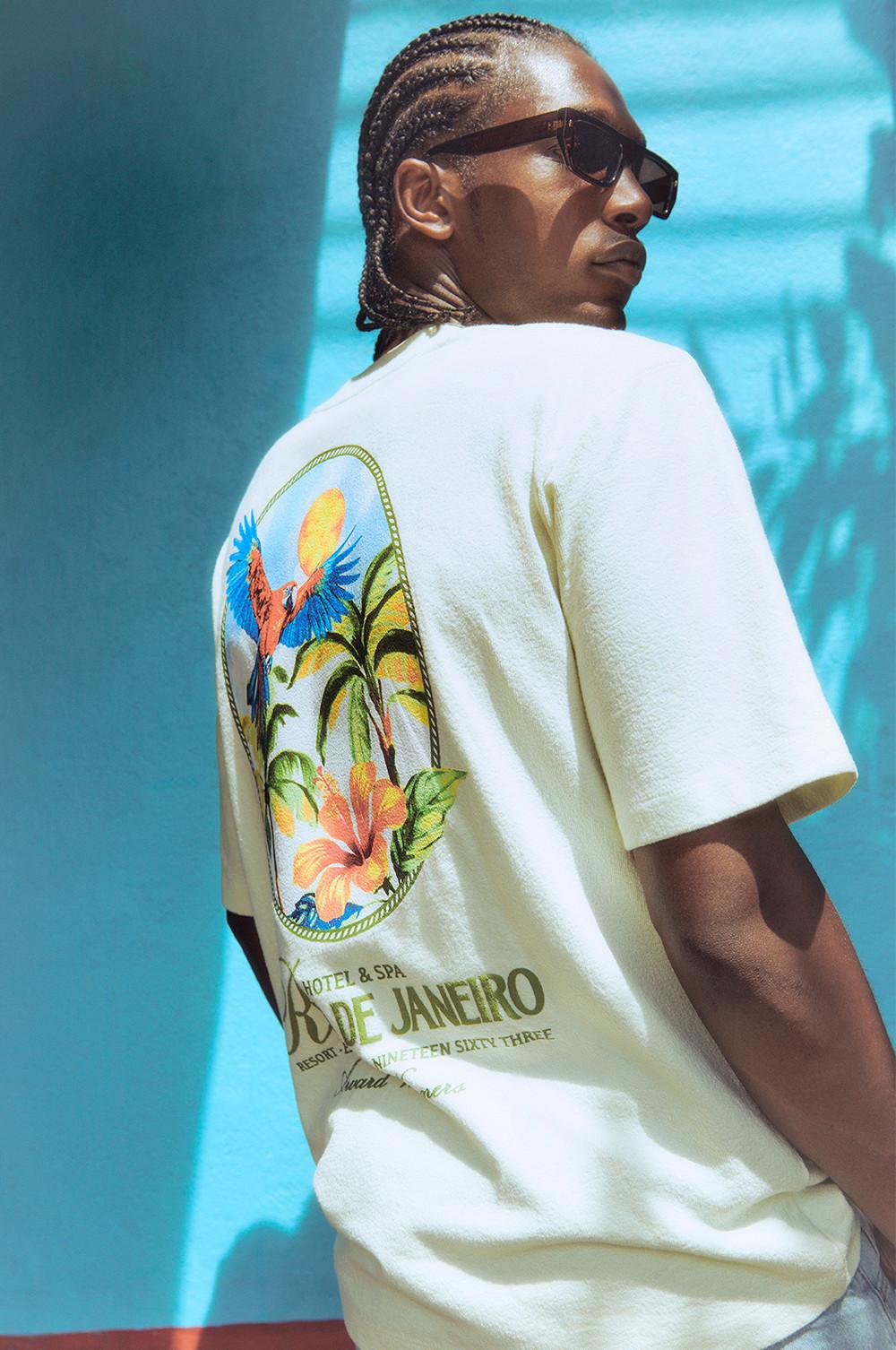 Modello che indossa una maglietta bianca con stampa tropicale sul retro, con pappagalli e palme