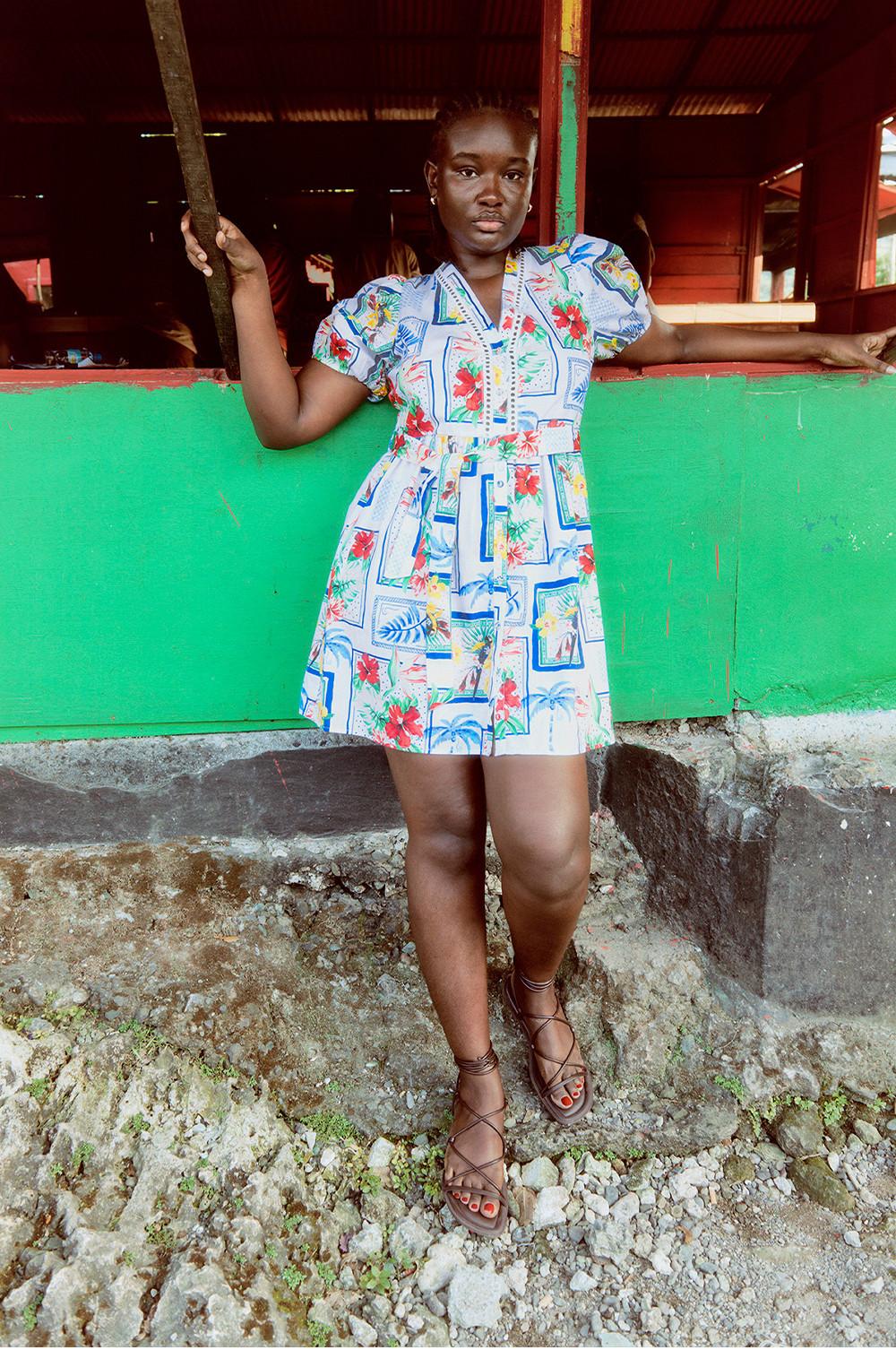 Modelo con vestido con estampado de postales y sandalias marrones con tiras.