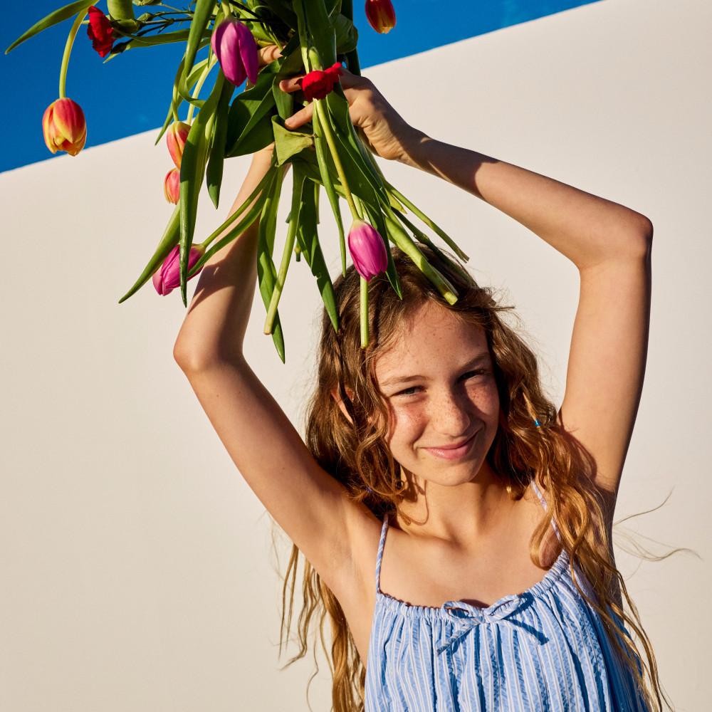 Personne portant un haut bleu à rayures et tenant des tulipes colorées au-dessus de sa tête, devant un fond de couleur vive.