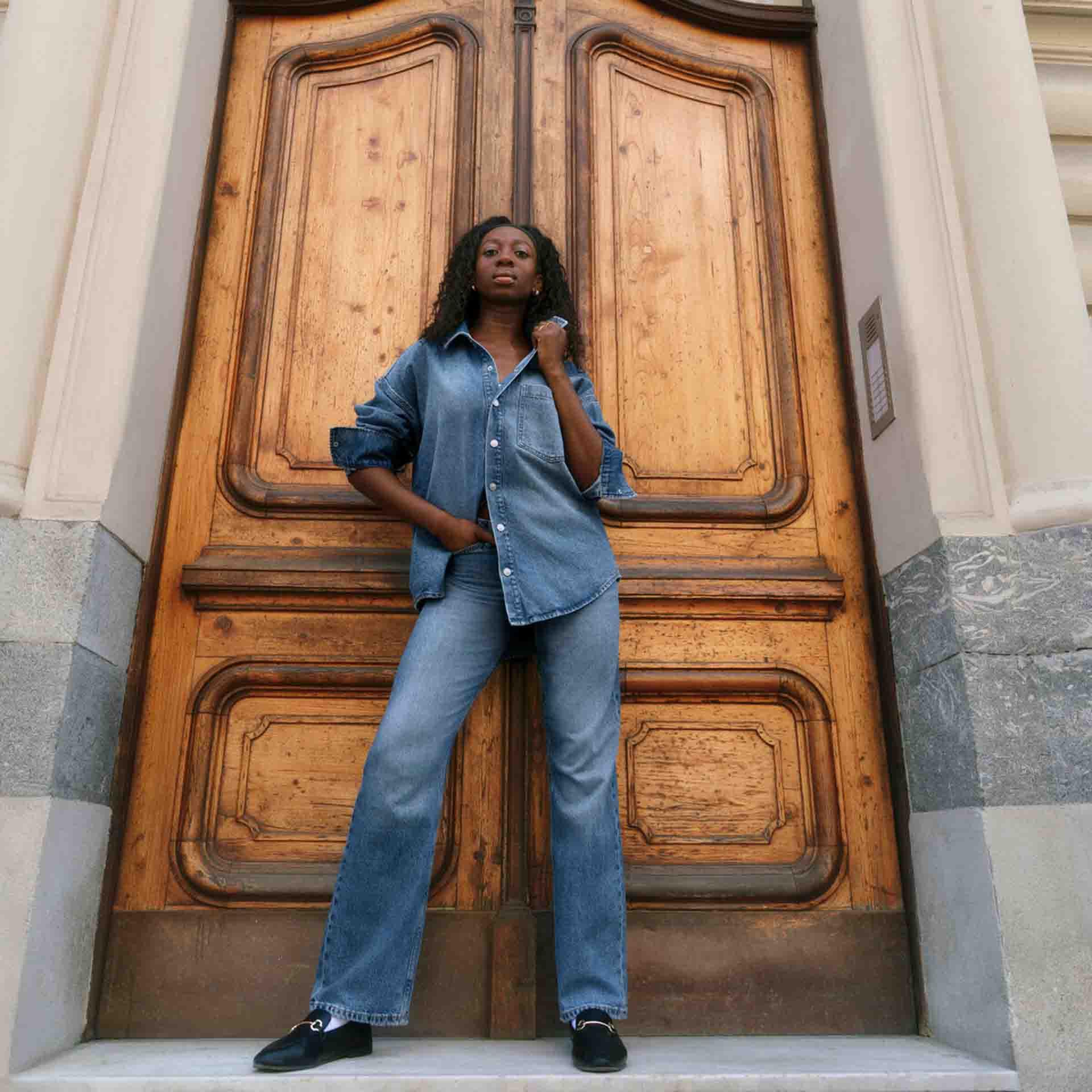 A female posing in front of wooden double doors wearing double denim from Primark.