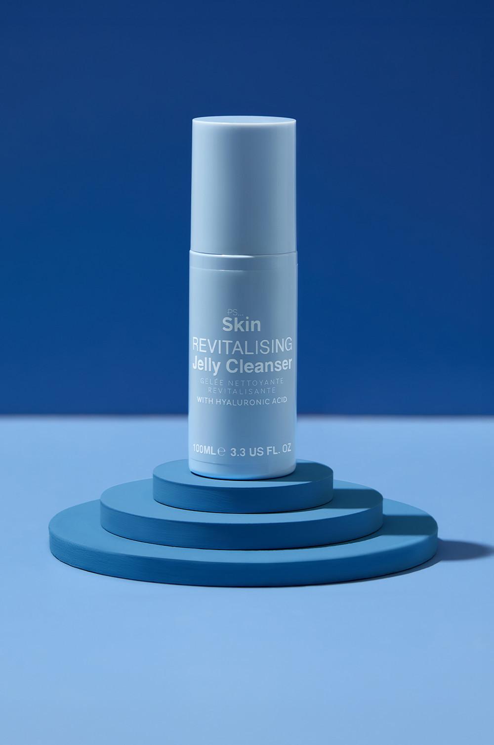 Gelée nettoyante revitalisante PS Skin bleu clair à l'acide hyaluronique présentée sur une plateforme bleue circulaire.