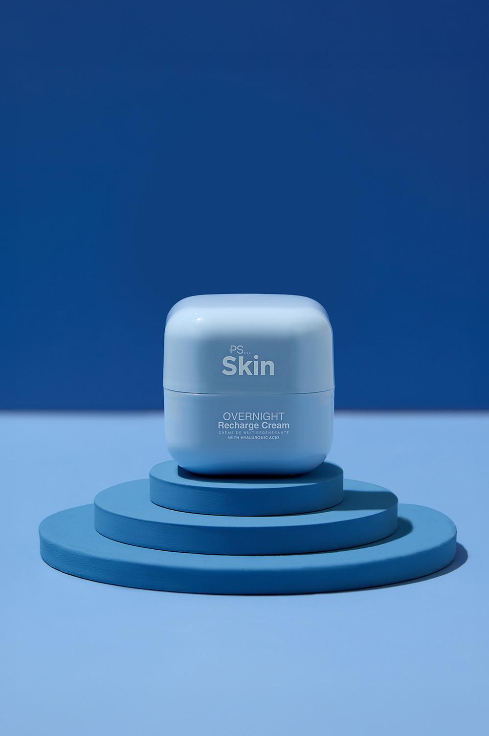 Crème de nuit Overnight Recharge PS Skin à l'acide hyaluronique dans un pot bleu clair, présentée sur une plateforme circulaire bleue.
