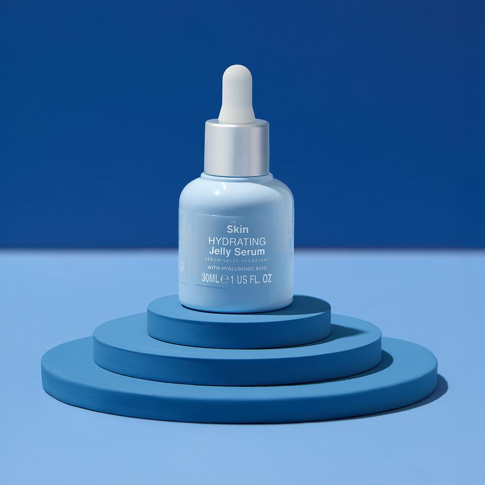 Flacon de sérum gelée hydratant bleu clair avec un compte-gouttes présenté sur une plateforme bleue à étages devant un fond bleu.