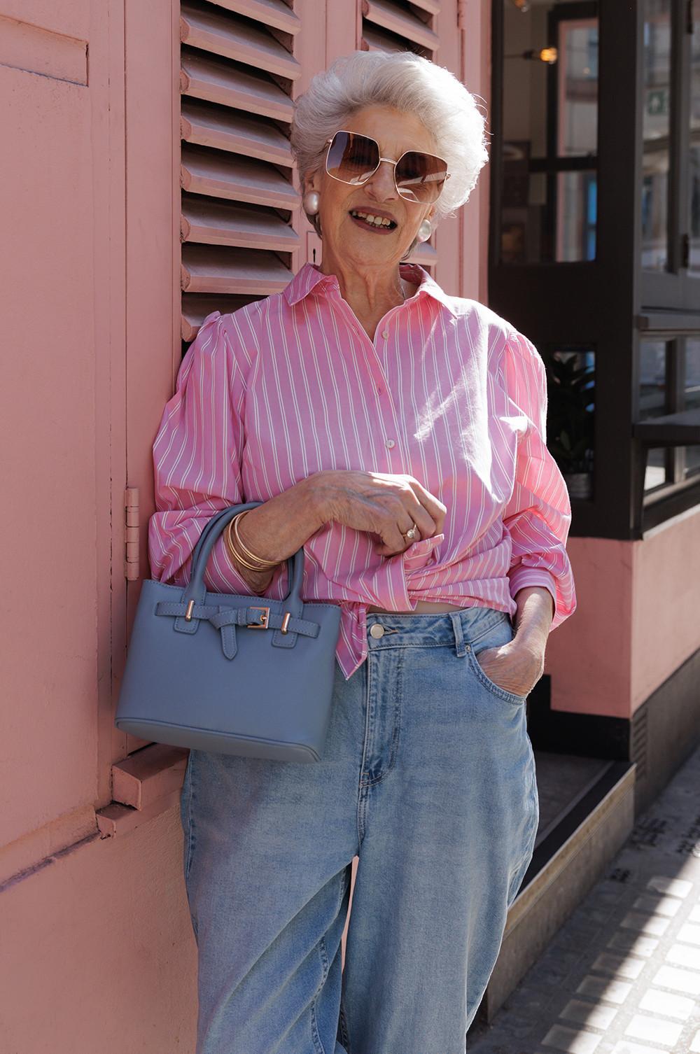 Model wearing a pink and white striped shirt, blue jeans and blue bag