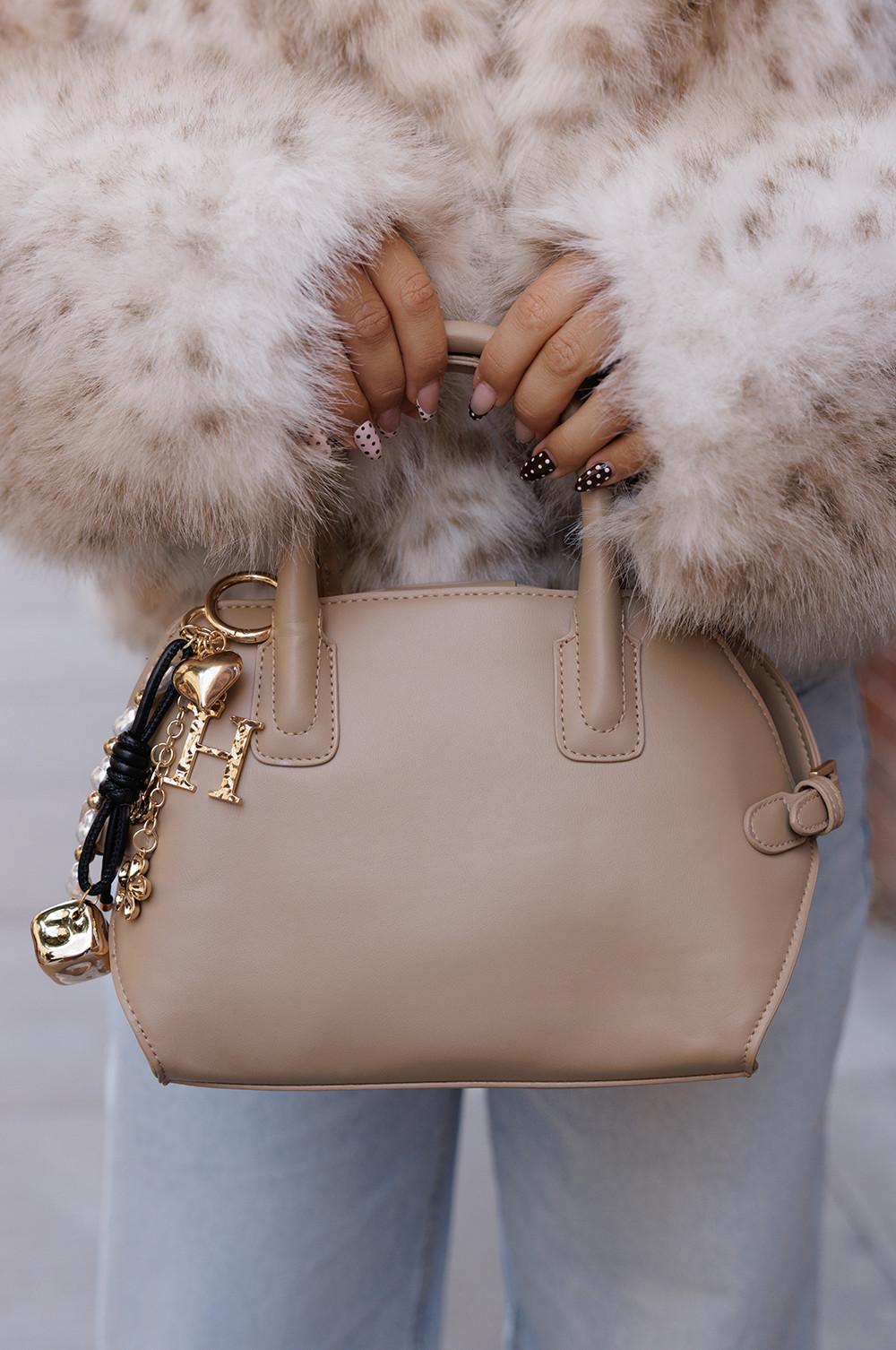 Mani con unghie a pois che reggono una borsa beige con ciondoli decorativi dorati mentre la modella indossa un cappotto di pelliccia.