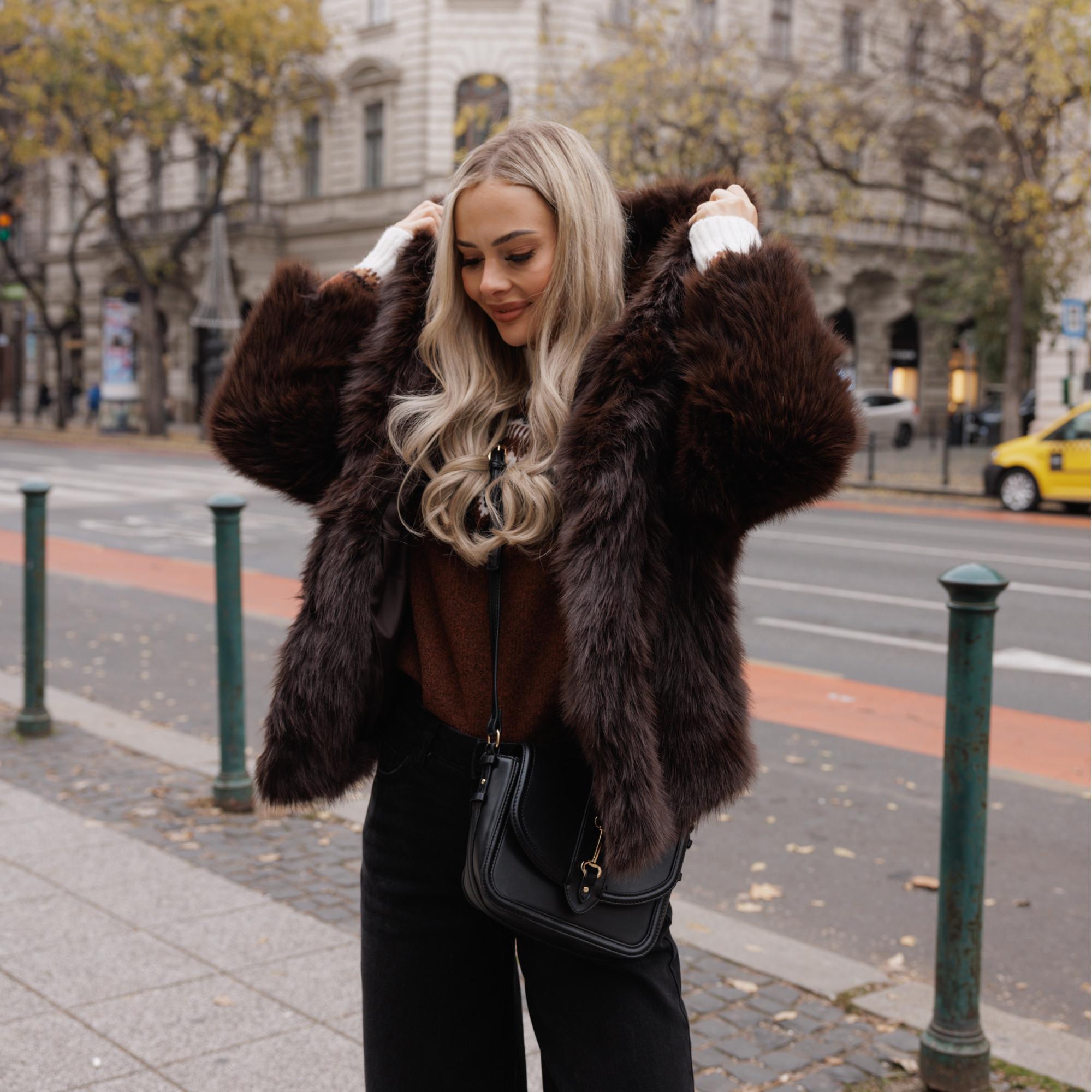 Person wearing luxurious brown fur coat with black trousers and crossbody bag on an autumn city street.