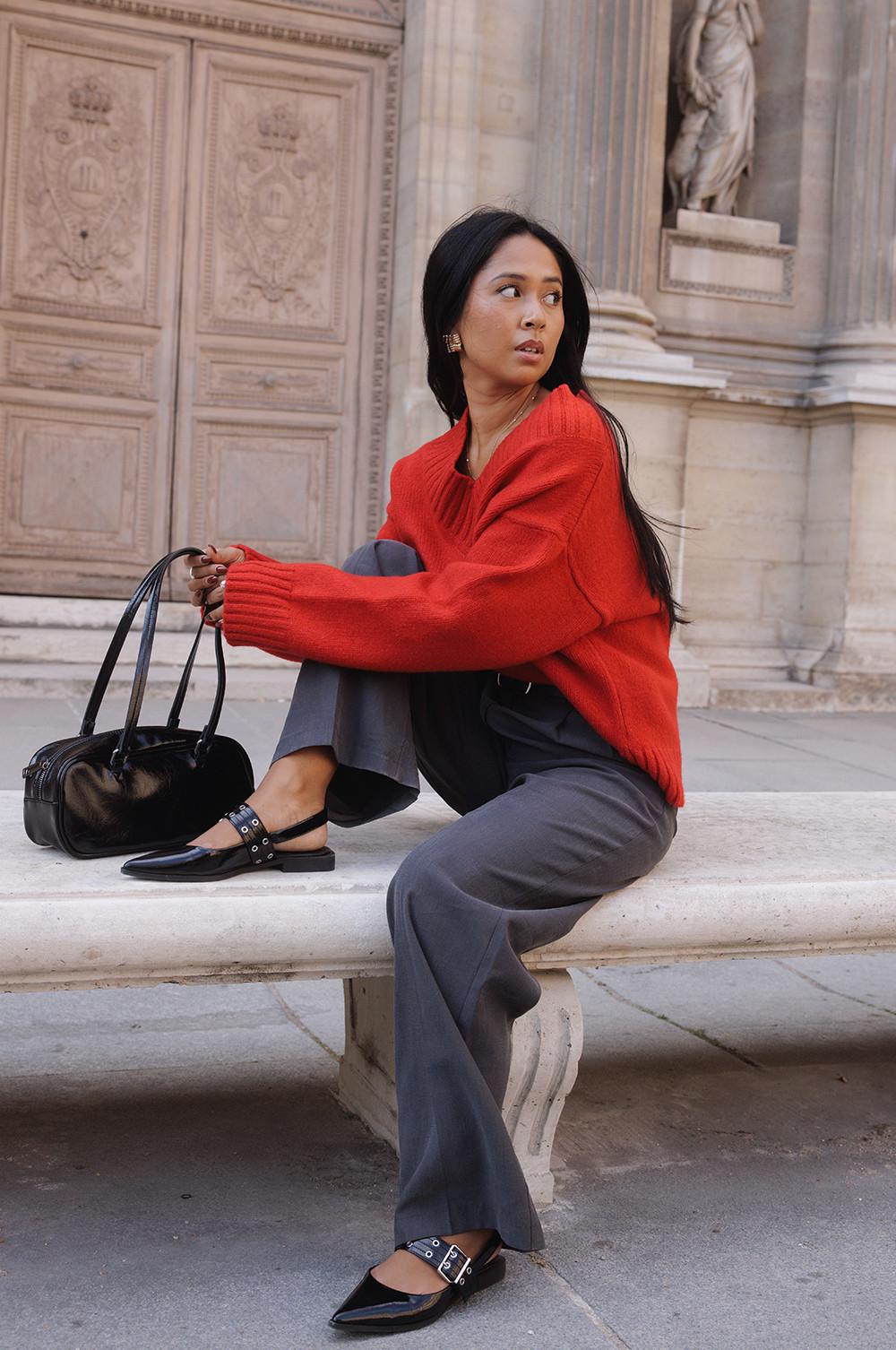 Donna che indossa un maglione rosso, pantaloni grigi, ballerine nere e una borsa