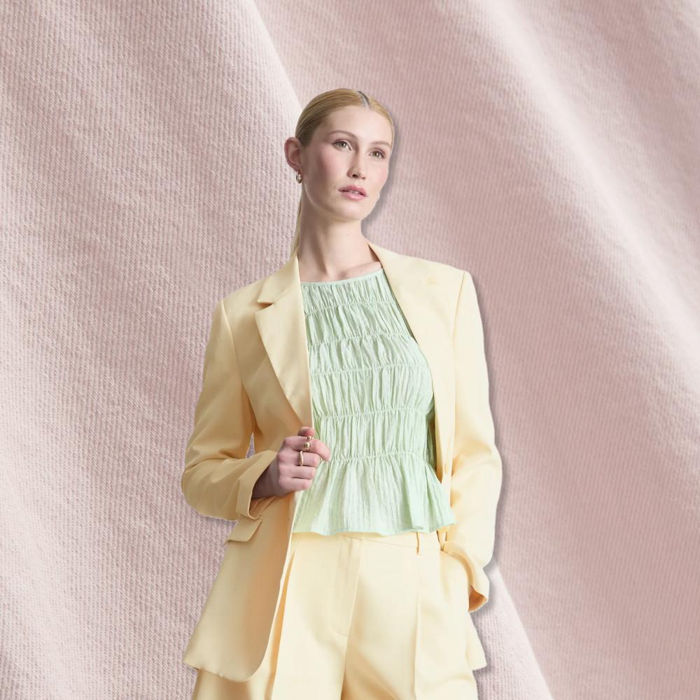 Modelo con un traje amarillo claro con un top verde menta texturizado, sobre un fondo de tela rosa suave.