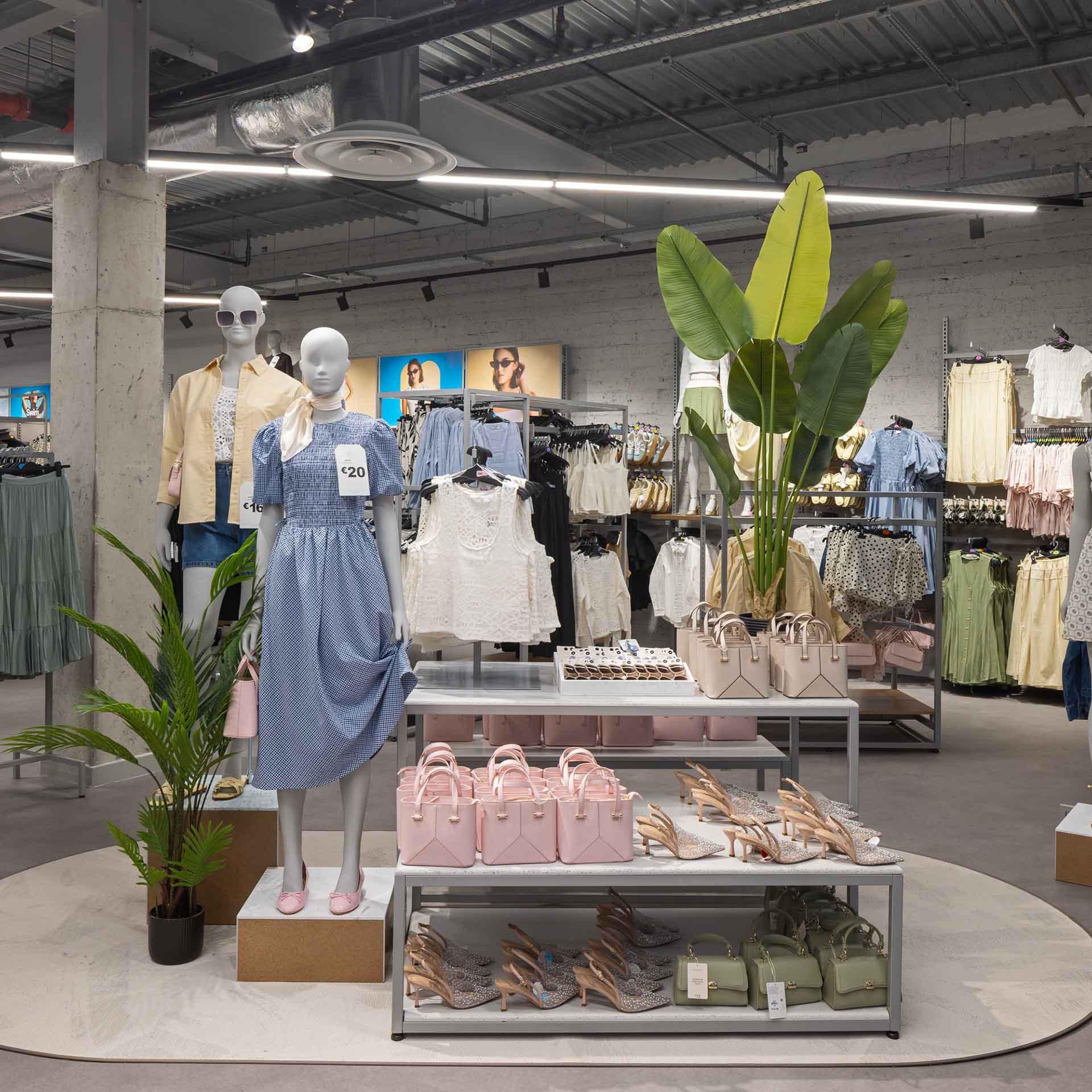 Store interior with two mannequins displaying summer dresses and racks of clothing.