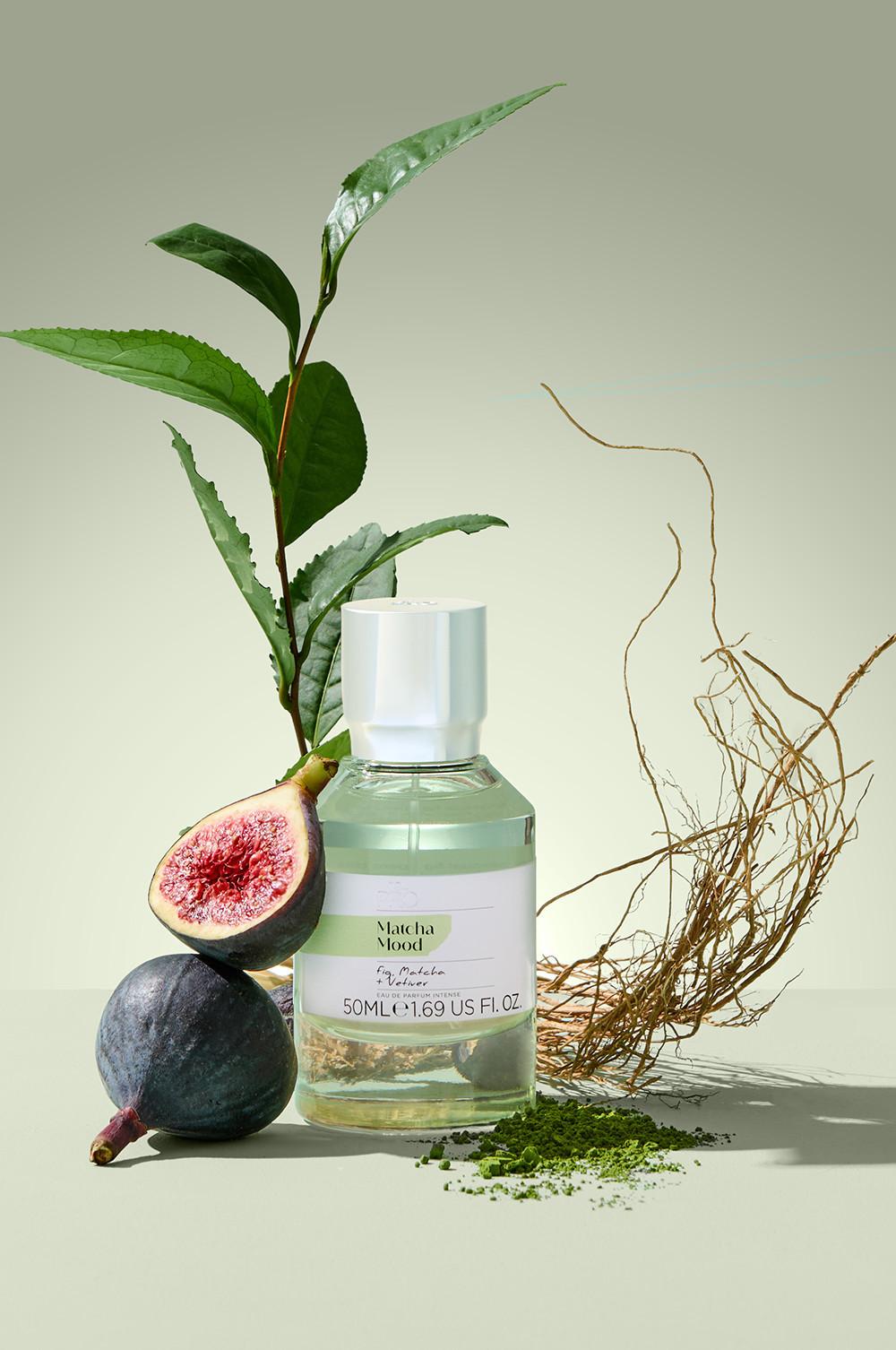 Flacon de parfum Matcha Mood présenté avec des figues fraîches, des feuilles de thé vert et une pincée de poudre verte.