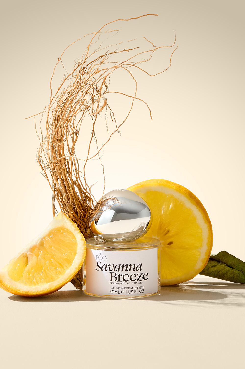 Flacon de parfum Savanna Breeze doté d'un bouchon argenté, présenté entouré de tranches de citrons et de racines de vétiver. Eau de parfum intense 30 ml.
