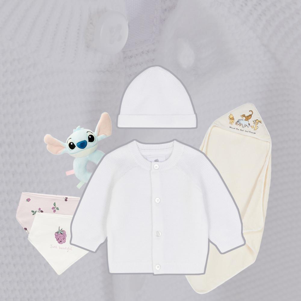 BabykIeidungs-Auswahl mit weißem Cardigan, Mütze, gemusterten Decken und Stitch-Plüschtier, auf hellem Hintergrund angeordnet.