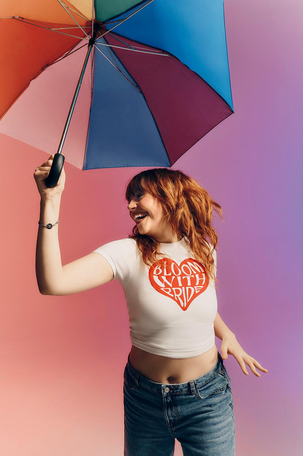 Modella che indossa una maglietta bianca “Bloom with pride” e tiene in mano un ombrello arcobaleno.