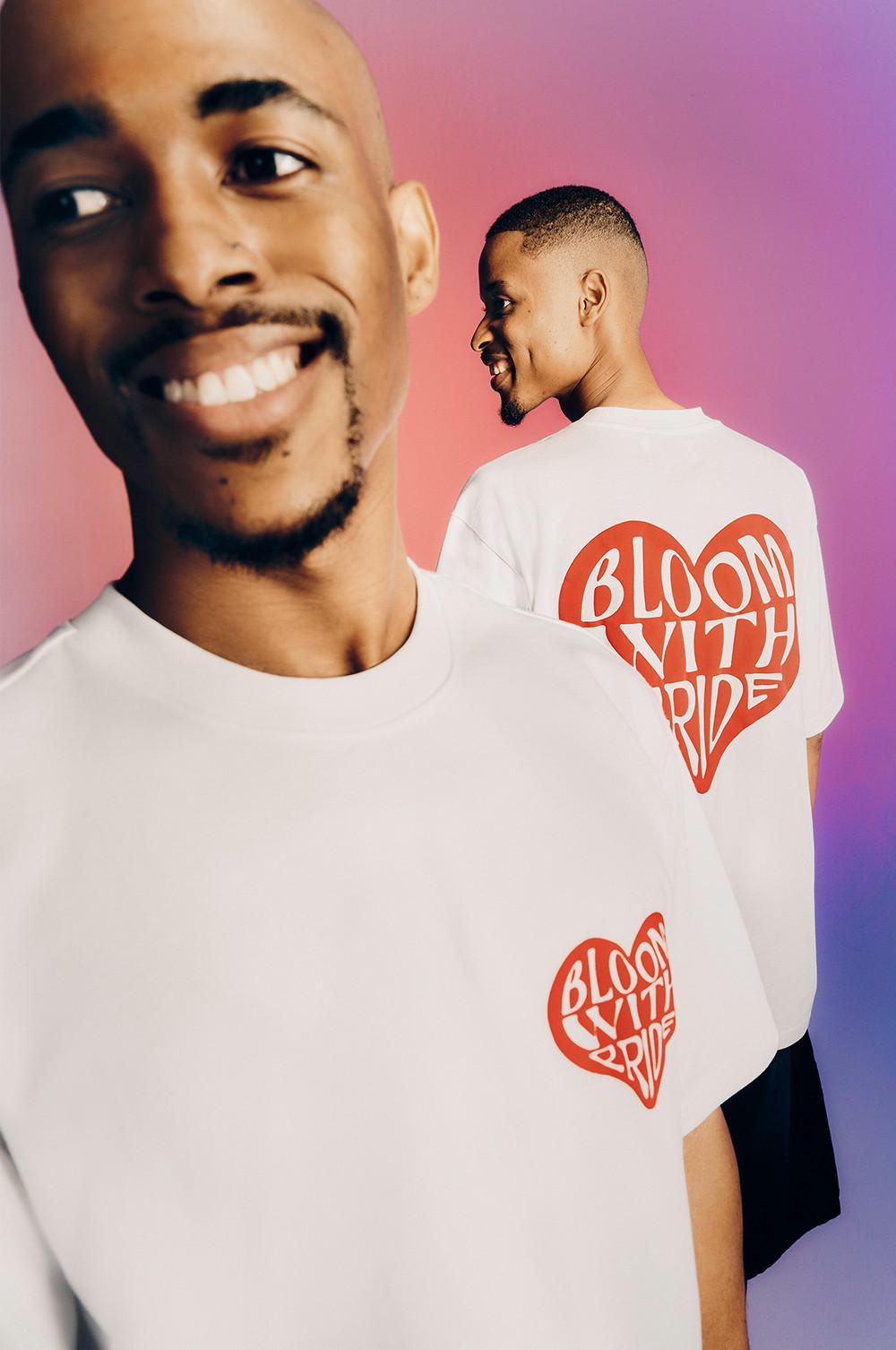 Modelli che indossano una maglietta bianca a maniche corte con il logo “Bloom with pride” sul davanti e sul retro.