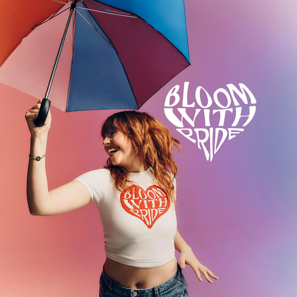 Modella che indossa una maglietta bianca con grafica "Bloom with pride" sul davanti