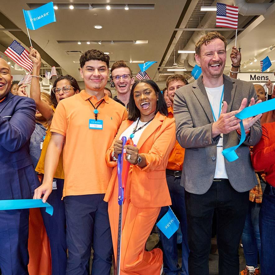 A Primark store opening with American and Primark flags as a woman cuts a blue ribbon.