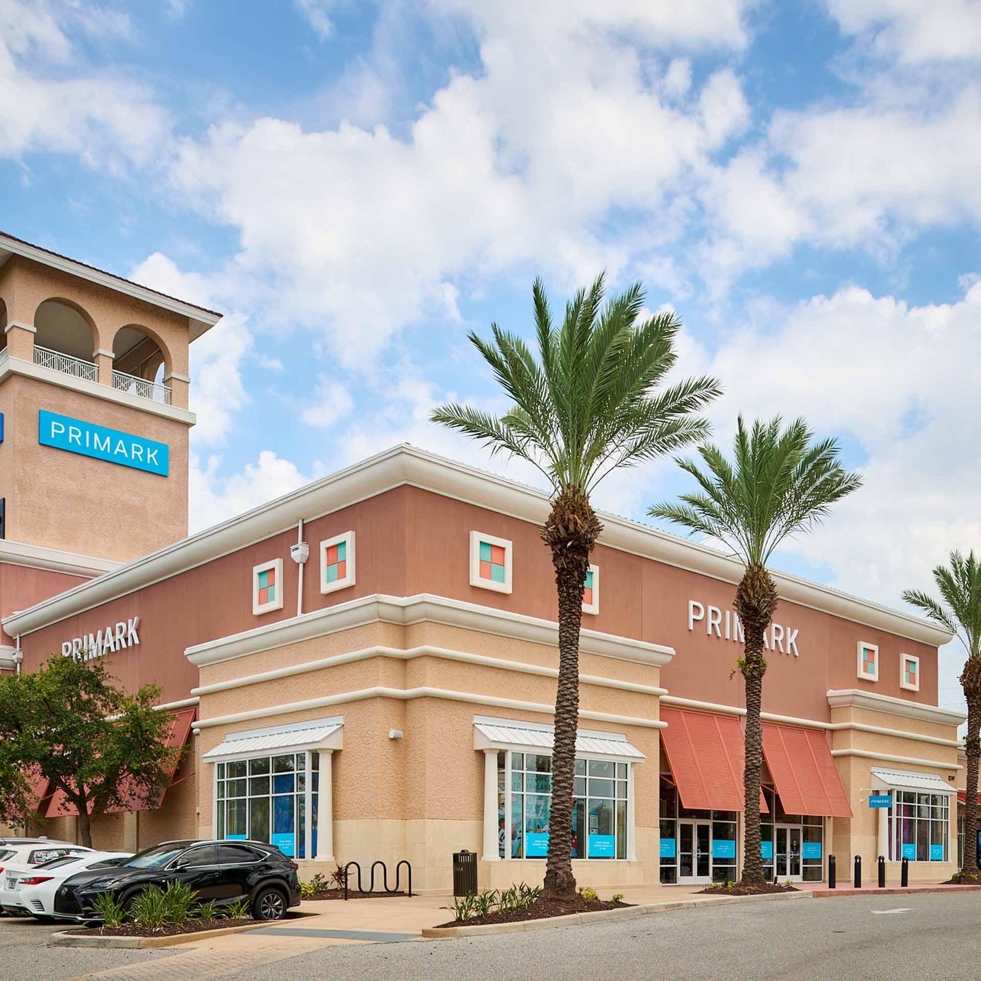 Primark store with tan walls, red awnings, palm trees and blue sky.