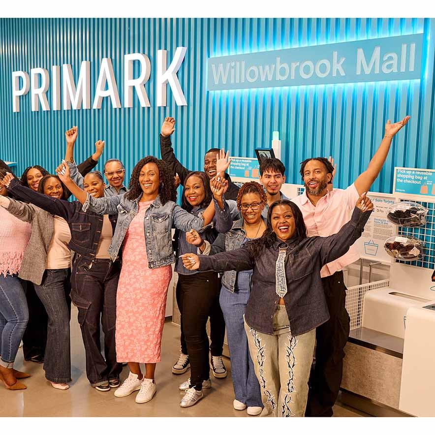 A diverse group of people celebrating in front of a Primark store sign at Willowbrook Mall.
