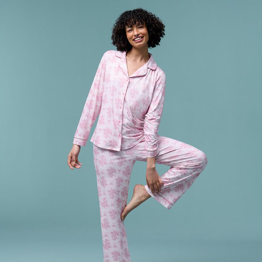 A woman with curly hair wears a light pink button-down pj set.