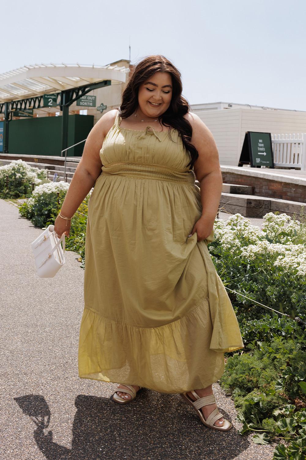 Light olive maxi dress with gathered waistline and tiered hem, paired with white handbag and sandals.