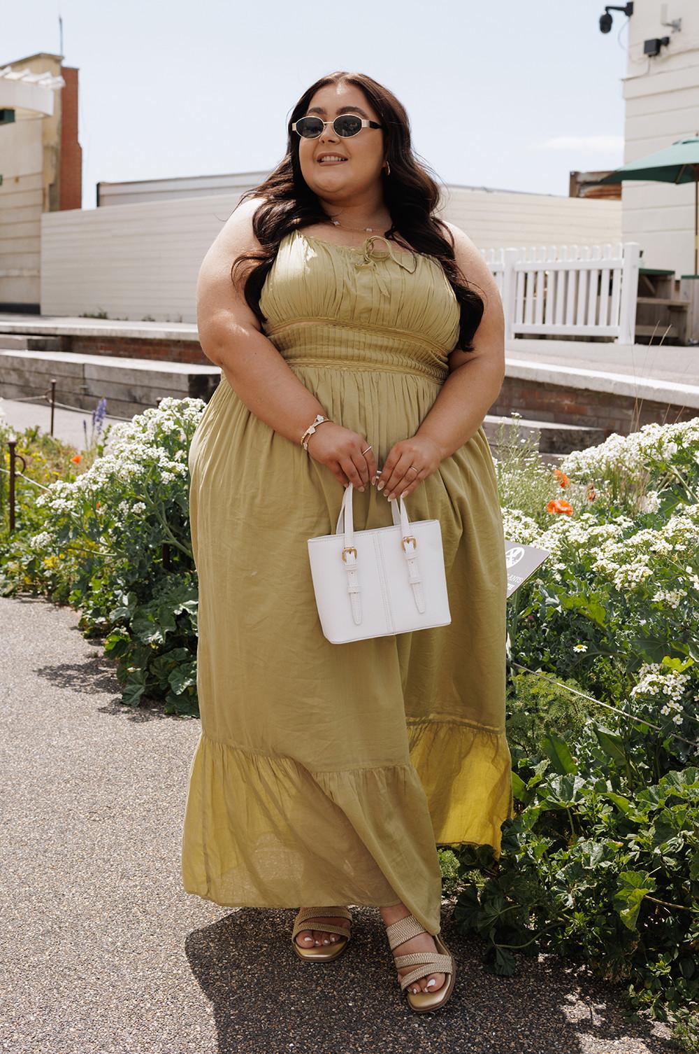Olive maxi dress with gathered waist and ruffle hem, paired with white mini handbag and sunglasses in garden setting.