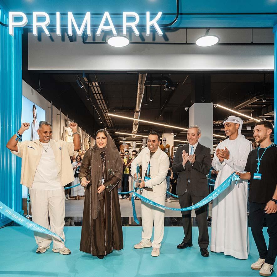 A diverse group of smiling people stand at a Primark store entrance for a ribbon-cutting ceremony.