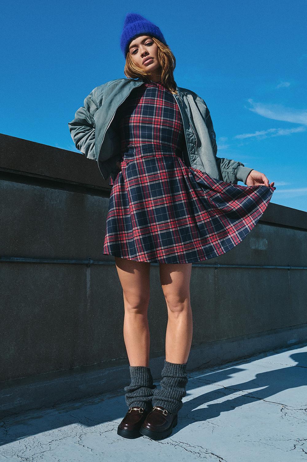 Model in Faltenkleid, grauer Bomberjacke, blauer Beanie und klobigen Loafern mit grauen Socken.