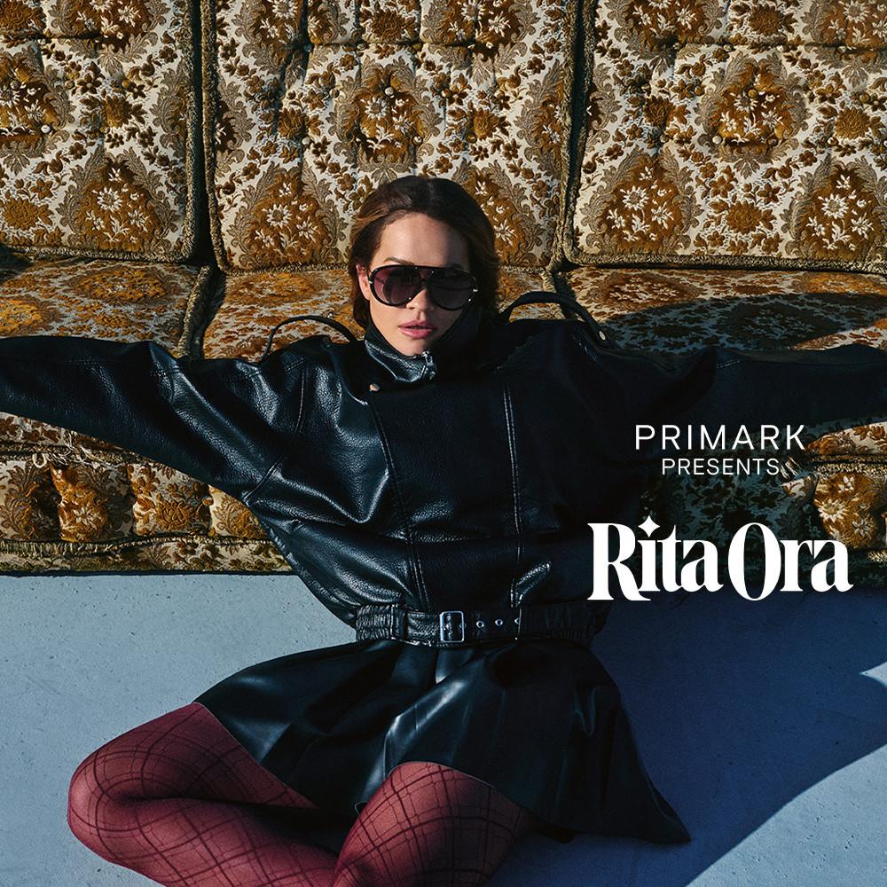 Model in schwarzem Lederoutfit mit roter Strumpfhose vor einem Sofa mit Vintage-Muster für die Rita Ora-Kollektion von Primark.