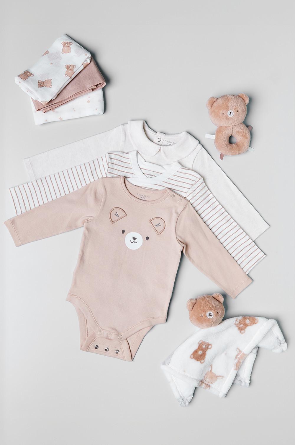 Baby-Kleidungsset mit Bodys, Decken und Plüschtieren mit Bärenmotiv in Weiß und Zartrosa.