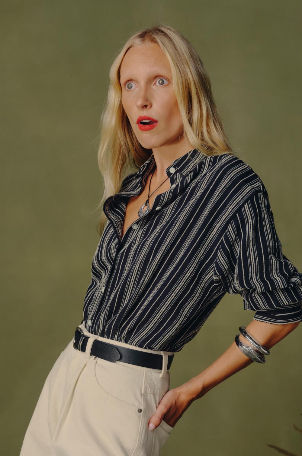 Modelo con camisa a rayas azul marino y blancas con manga de tres cuartos, combinada con pantalones color crema.