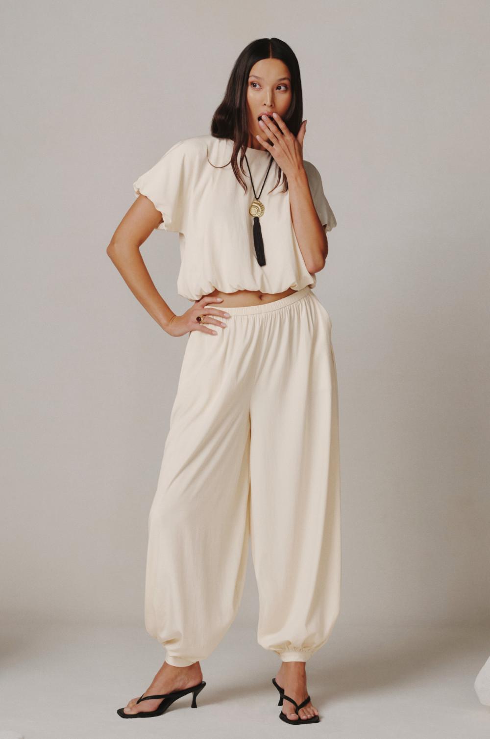 Modelo con top de manga corta color crema, collar tipo bolo, pantalones de pernera ancha a juego y sandalias de tacón negras.