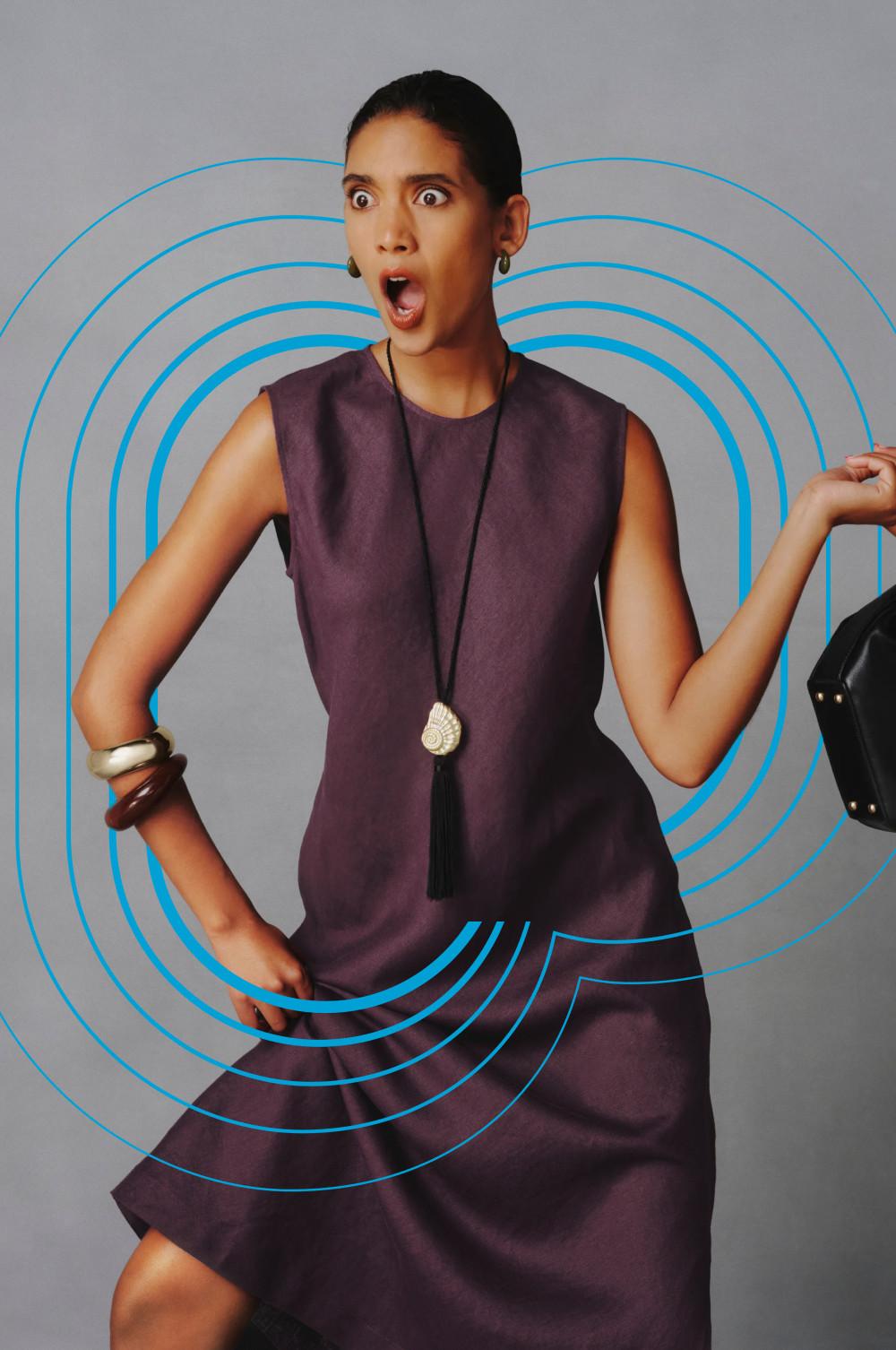 Modelo con gesto de sorpresa con un vestido sin mangas de color morado, un collar con borlas y brazaletes metalizados.
