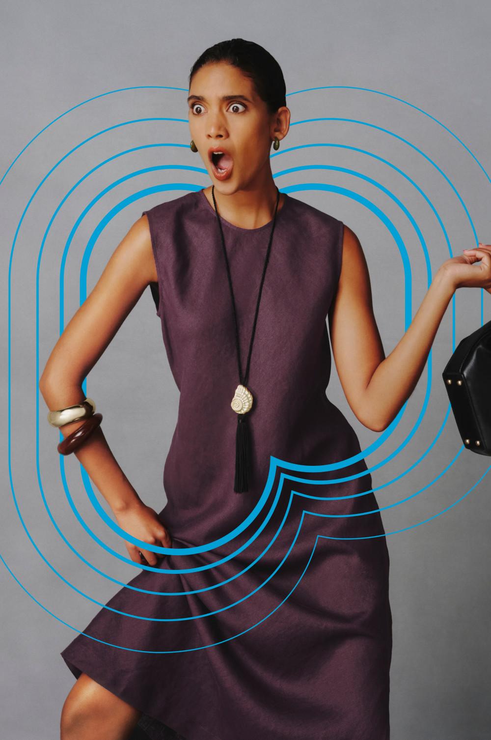 Model expressing shock in purple sleeveless linen dress with tassel necklace and metallic bangles.