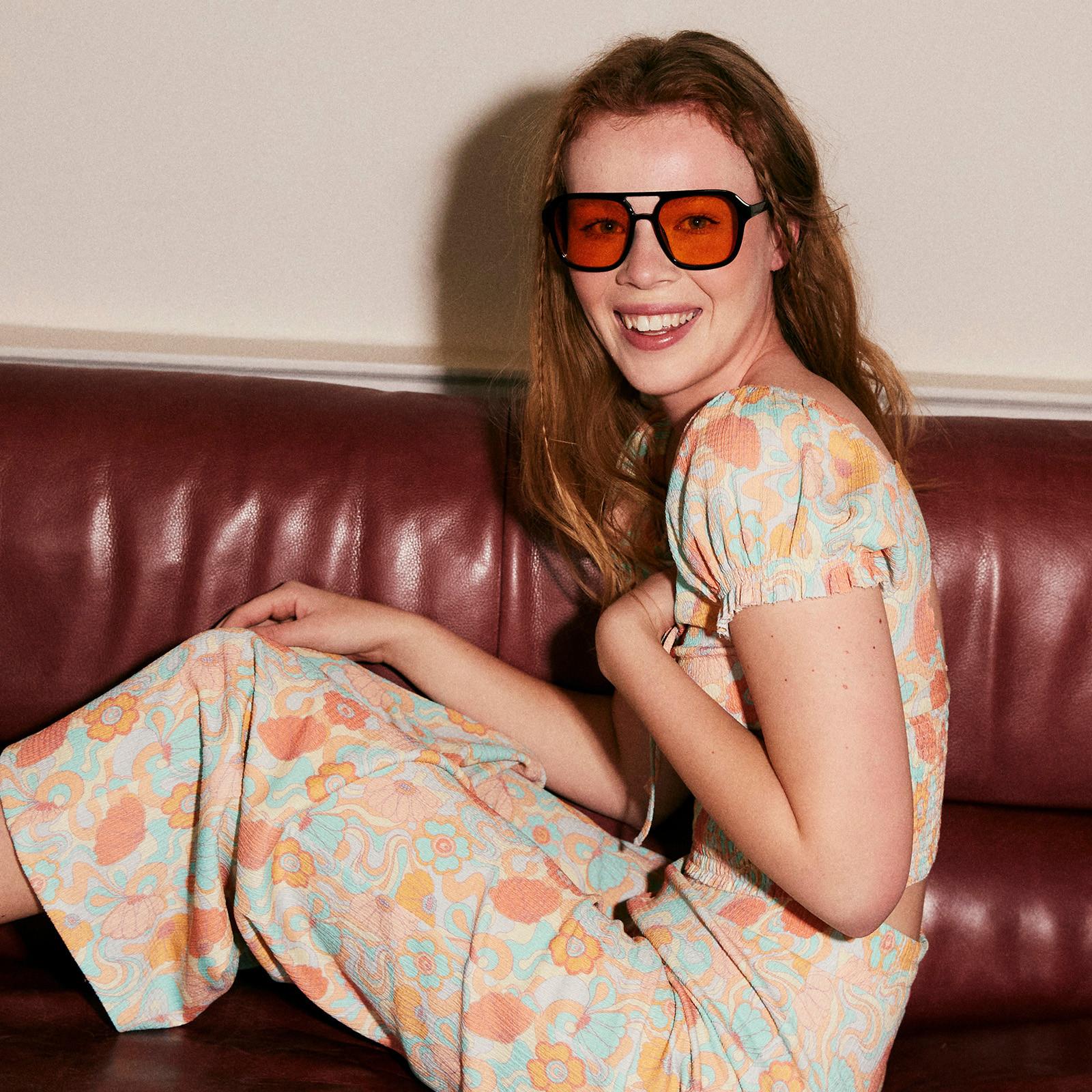 Model wears floral two piece with large tinted sunglasses