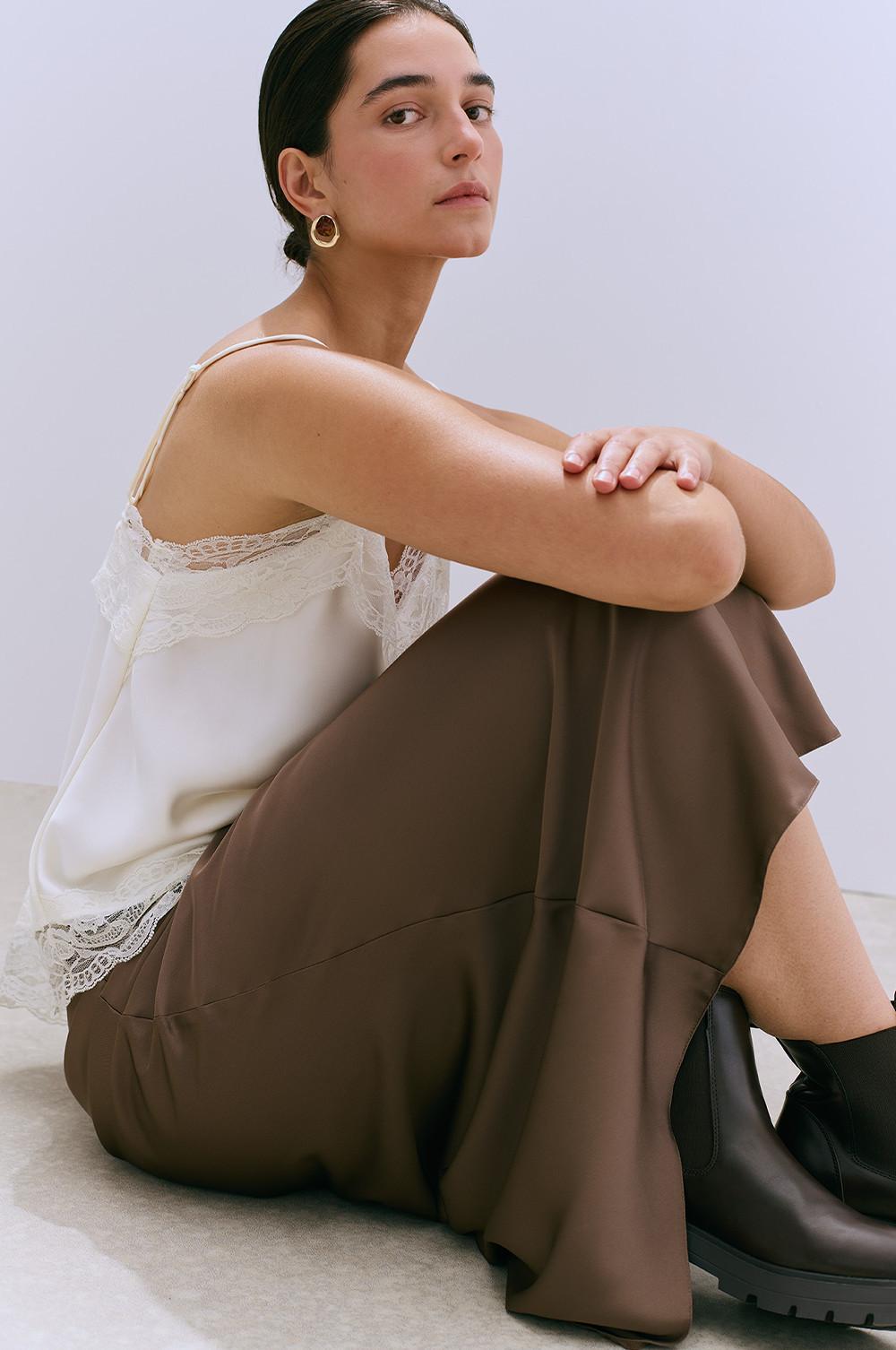 Person wearing cream lace-trimmed camisole with brown wide-leg trousers and black boots, gold hoop earrings.