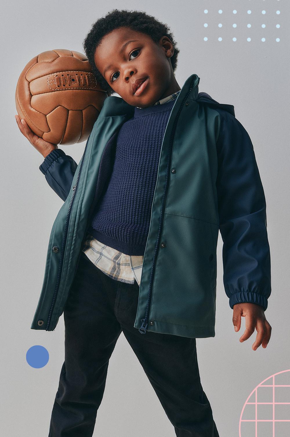 Child wearing green jacket and navy sweater holding a vintage-style leather ball.
