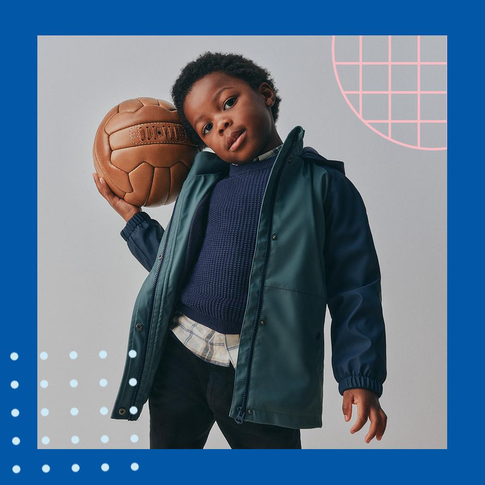 Child wearing green jacket and navy sweater holding a vintage-style leather ball.