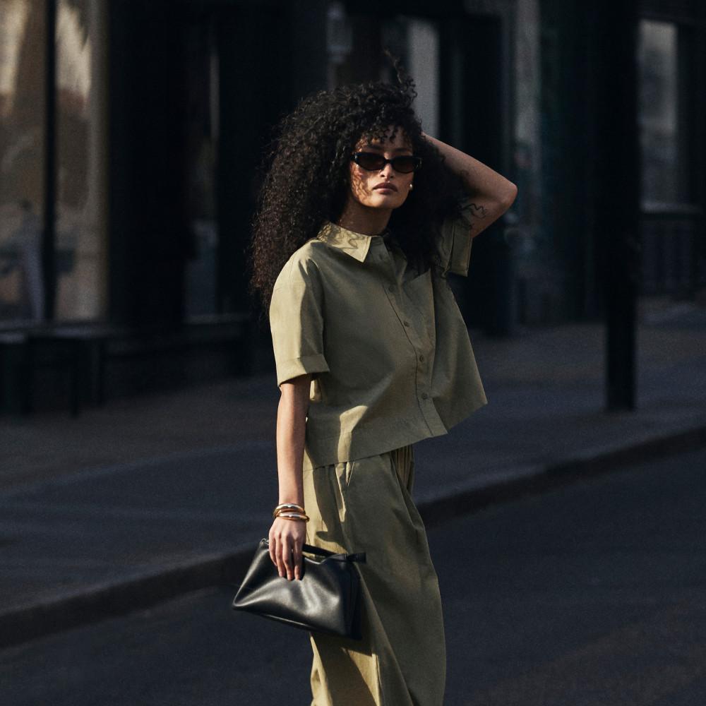 Person wearing brown jacket and trousers with sunglasses standing on stone steps, featured in SHEERLUXE.